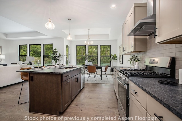 kitchen with wall chimney exhaust hood, a kitchen bar, sink, a raised ceiling, and stainless steel appliances