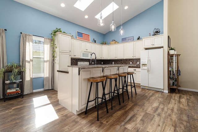 kitchen with a skylight, a breakfast bar area, white cabinets, a kitchen island with sink, and white appliances