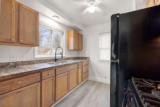 kitchen featuring sink, light hardwood / wood-style flooring, black refrigerator, gas stove, and dark stone counters