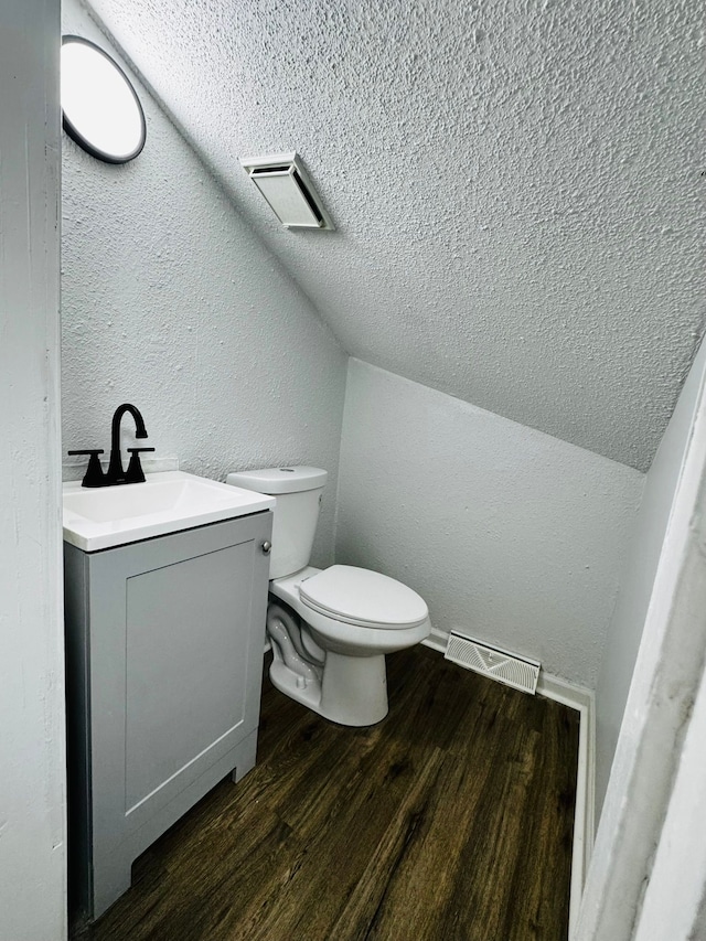 bathroom with hardwood / wood-style flooring, vanity, a textured ceiling, vaulted ceiling, and toilet