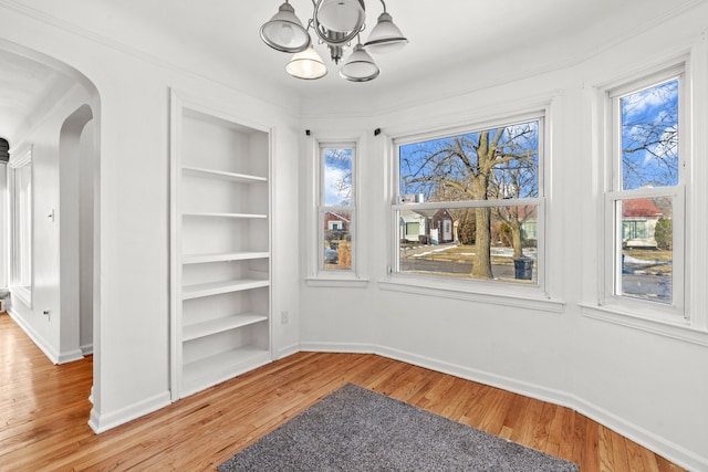 unfurnished dining area featuring built in shelves, a chandelier, light hardwood / wood-style flooring, and a wealth of natural light