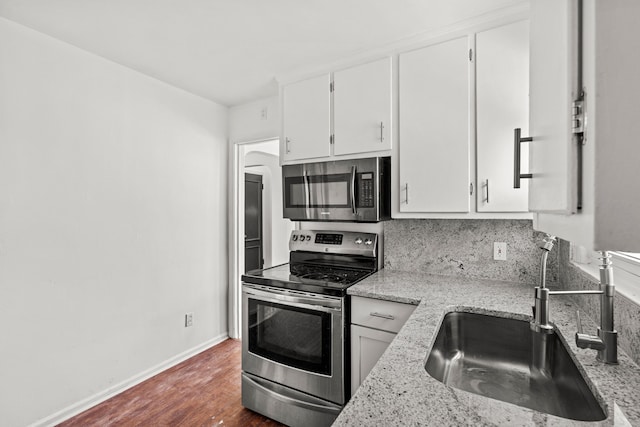 kitchen featuring stainless steel appliances, white cabinetry, sink, and light stone counters