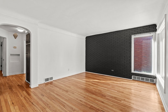 unfurnished room with light hardwood / wood-style floors and brick wall