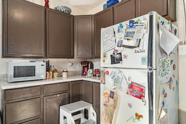 kitchen with white appliances, light countertops, and dark brown cabinetry