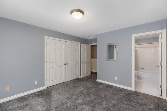 unfurnished bedroom featuring ensuite bath, dark carpet, and a closet