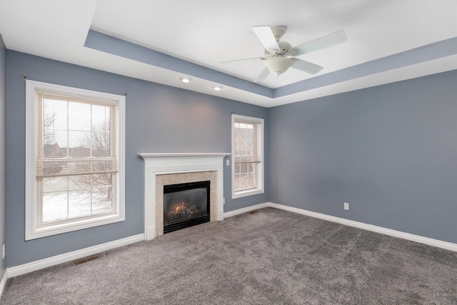 unfurnished living room featuring a raised ceiling, dark colored carpet, and ceiling fan