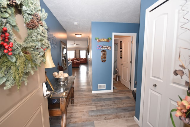 hall featuring visible vents, dark wood finished floors, a textured ceiling, and baseboards