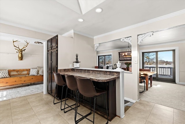 kitchen featuring a breakfast bar area, dark brown cabinets, light carpet, ornamental molding, and kitchen peninsula