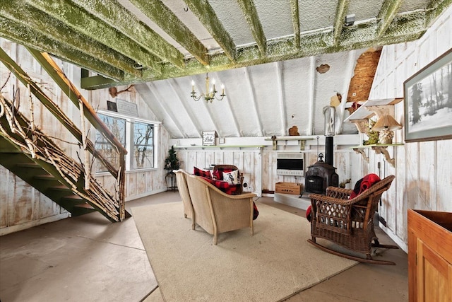 living room with lofted ceiling, concrete flooring, a chandelier, and a wood stove