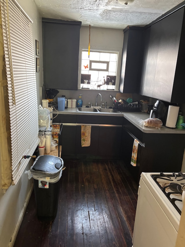 kitchen with a sink, gas range gas stove, dark wood-style flooring, and a textured ceiling