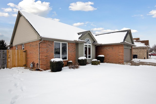 snow covered house with a garage, fence, and brick siding