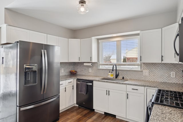 kitchen with appliances with stainless steel finishes, a sink, white cabinetry, and light stone countertops