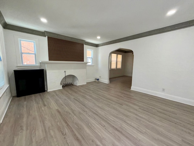 unfurnished living room featuring ornamental molding, a brick fireplace, and light wood-type flooring