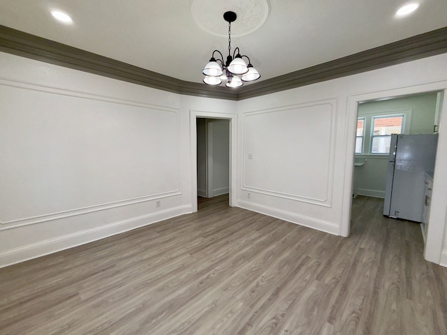 unfurnished dining area with an inviting chandelier, ornamental molding, and wood-type flooring