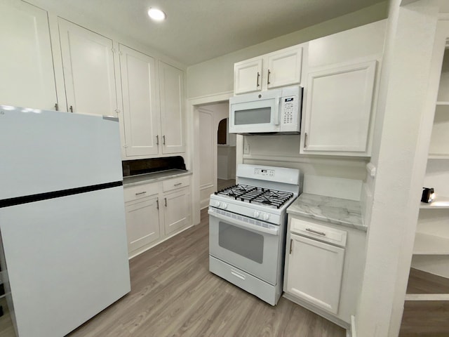 kitchen with light stone counters, white appliances, white cabinets, and light wood-type flooring