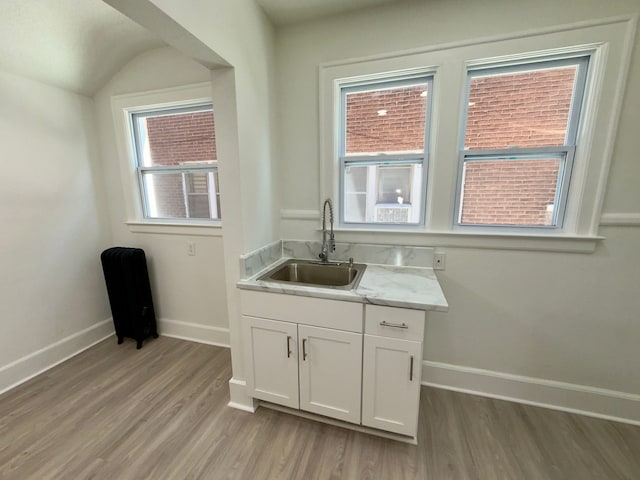 kitchen with light hardwood / wood-style floors, sink, light stone countertops, and white cabinets