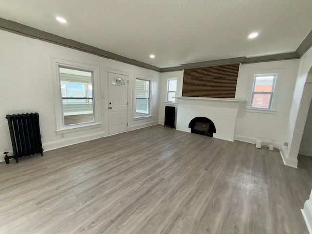 unfurnished living room featuring radiator, light hardwood / wood-style flooring, ornamental molding, and a brick fireplace