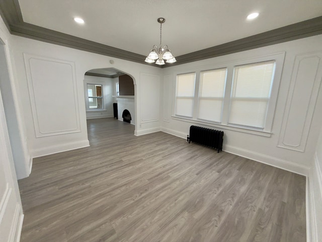 unfurnished dining area featuring ornamental molding, radiator heating unit, a chandelier, and hardwood / wood-style floors