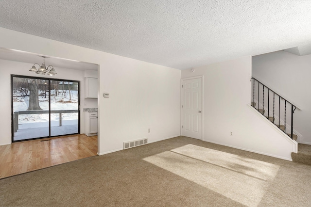 carpeted empty room featuring a notable chandelier and a textured ceiling