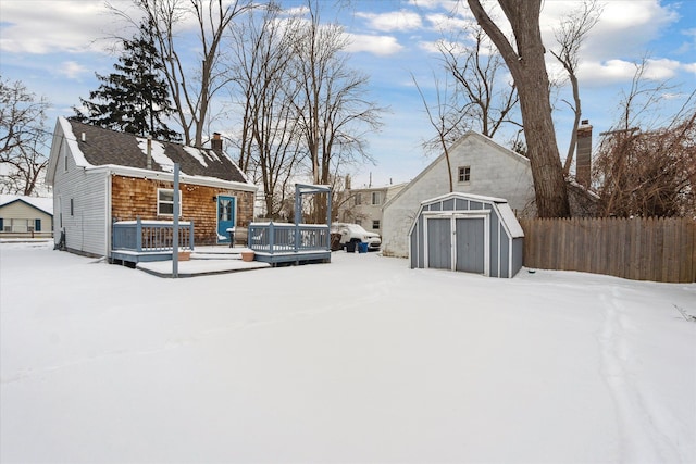 yard layered in snow featuring a wooden deck and a storage unit