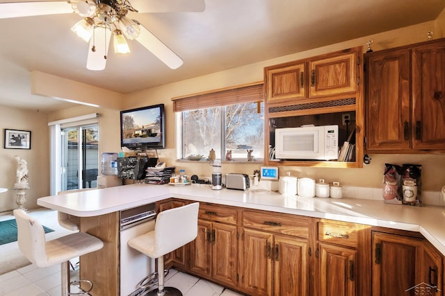 kitchen featuring light tile patterned floors, kitchen peninsula, ceiling fan, and a kitchen bar