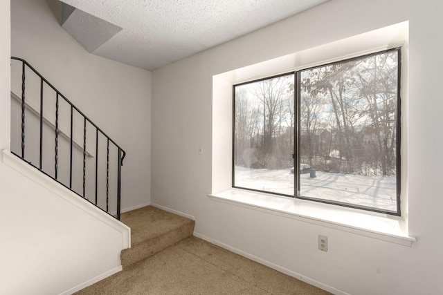 stairs featuring a healthy amount of sunlight, carpet, and a textured ceiling