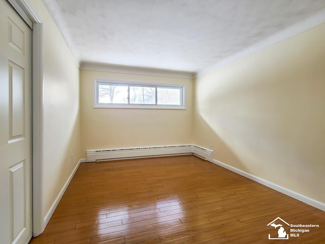 unfurnished room with hardwood / wood-style flooring and a baseboard heating unit