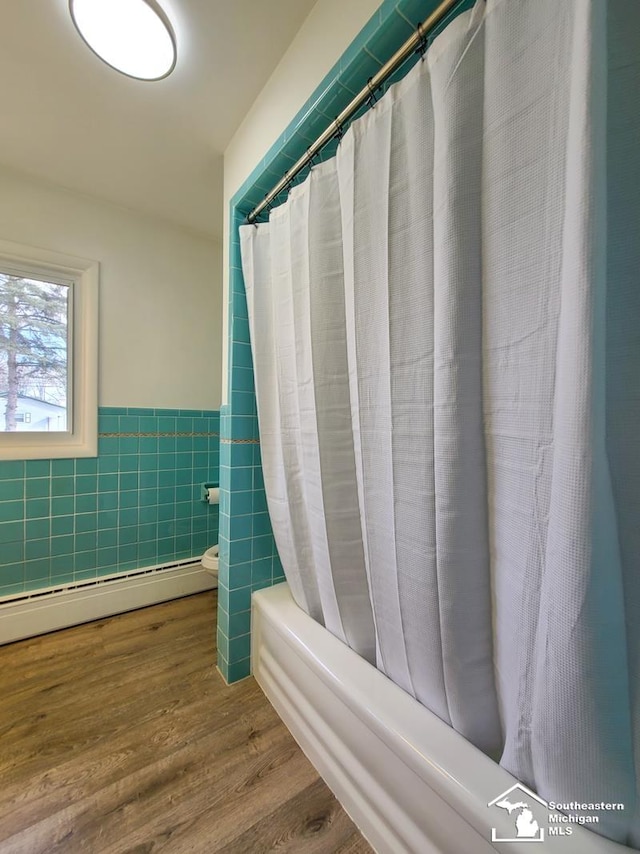 bathroom featuring toilet, shower / tub combo, tile walls, hardwood / wood-style flooring, and a baseboard heating unit