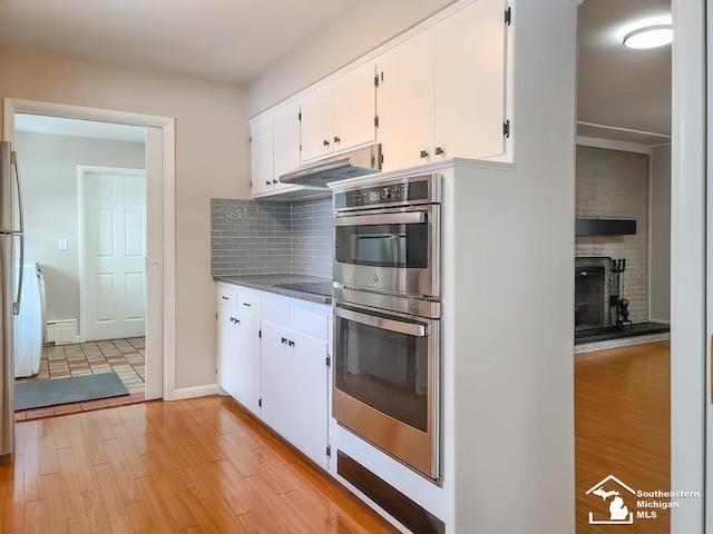 kitchen featuring double oven, white cabinets, backsplash, black electric stovetop, and light hardwood / wood-style flooring