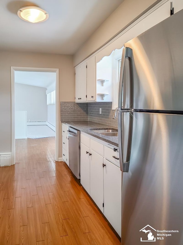 kitchen with appliances with stainless steel finishes, white cabinetry, sink, dark stone counters, and light hardwood / wood-style flooring