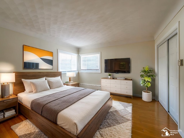 bedroom with hardwood / wood-style floors, a closet, and a baseboard heating unit