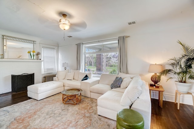 living room with hardwood / wood-style flooring, ceiling fan, radiator heating unit, and a fireplace