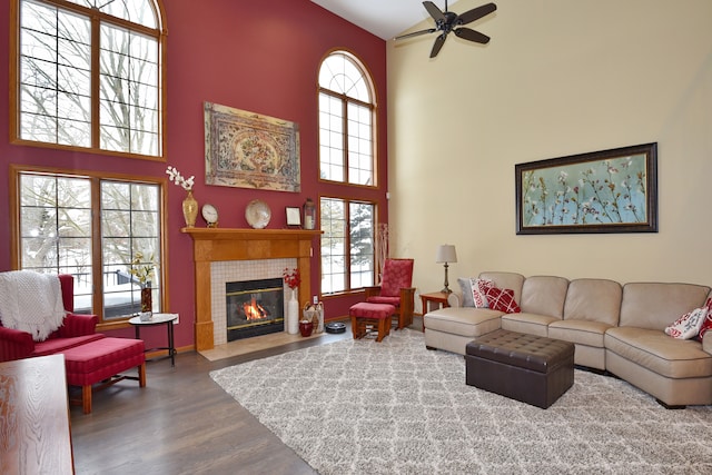 living area with a ceiling fan, a tile fireplace, a towering ceiling, and wood finished floors