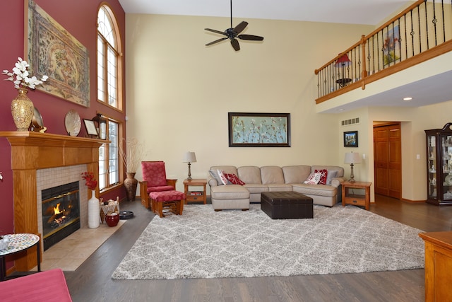 living room featuring a towering ceiling, a tiled fireplace, wood finished floors, and visible vents