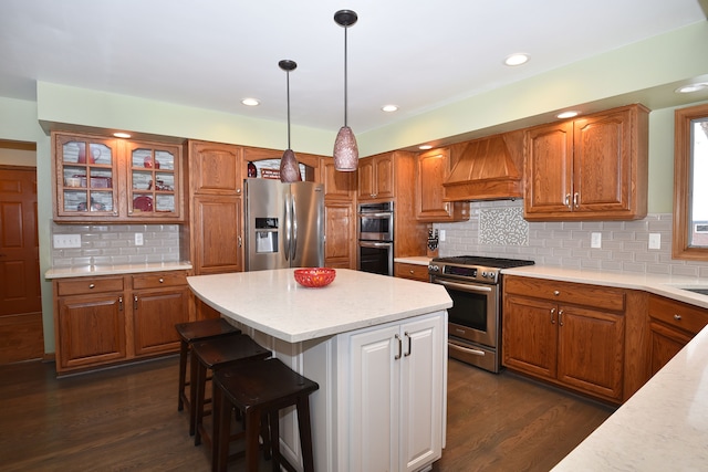 kitchen featuring appliances with stainless steel finishes, custom exhaust hood, decorative light fixtures, and brown cabinets