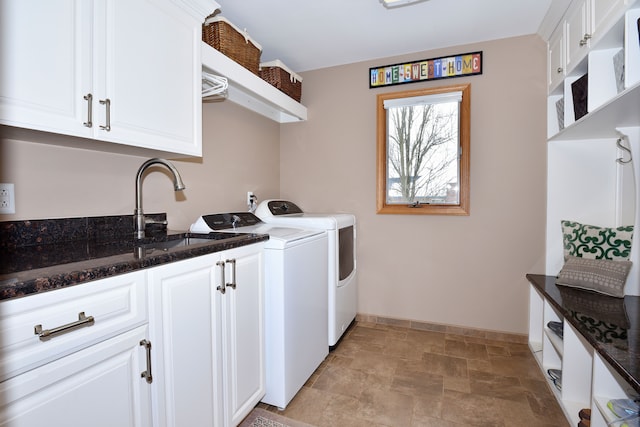 clothes washing area featuring cabinet space, baseboards, stone finish floor, washing machine and dryer, and a sink