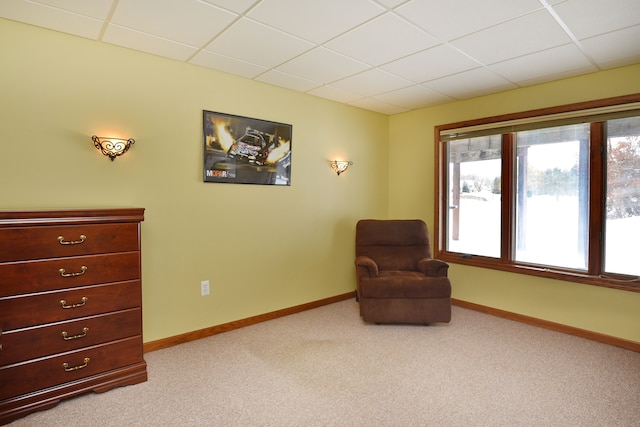 sitting room with baseboards, a drop ceiling, and light colored carpet