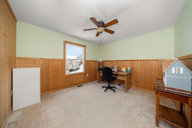 carpeted office space featuring ceiling fan and wood walls