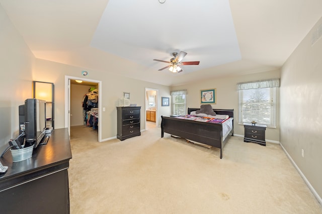 bedroom featuring ensuite bathroom, a walk in closet, light carpet, and a tray ceiling