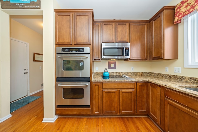 kitchen featuring stainless steel appliances, light stone countertops, and light wood-type flooring