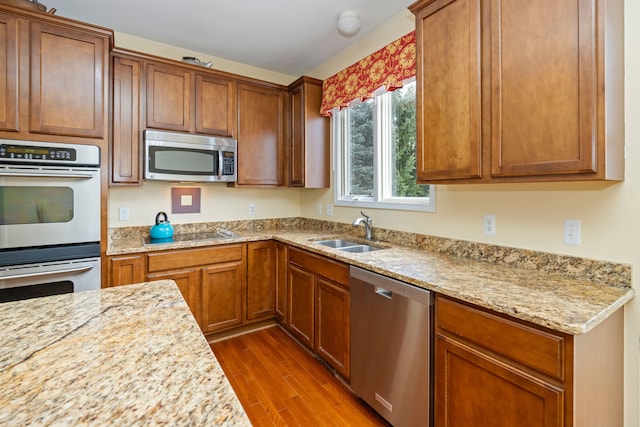 kitchen featuring light stone countertops, appliances with stainless steel finishes, sink, and hardwood / wood-style floors