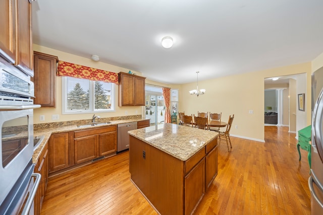 kitchen featuring appliances with stainless steel finishes, a kitchen island, decorative light fixtures, sink, and light hardwood / wood-style floors