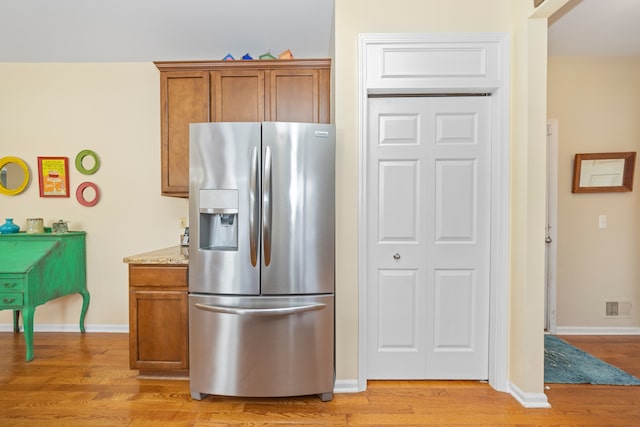 kitchen with stainless steel refrigerator with ice dispenser, light stone countertops, and light hardwood / wood-style flooring