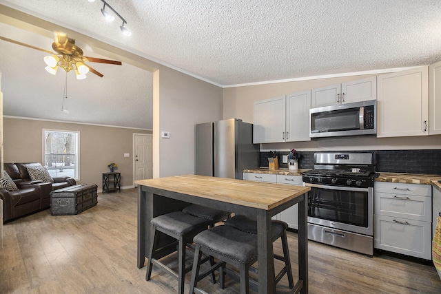 kitchen with ceiling fan, stainless steel appliances, ornamental molding, light hardwood / wood-style floors, and a textured ceiling