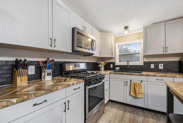 kitchen with appliances with stainless steel finishes, sink, wooden counters, white cabinets, and hardwood / wood-style flooring