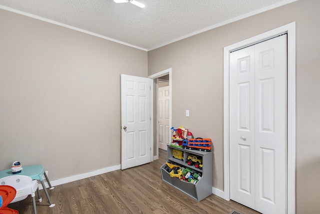 game room featuring dark wood-type flooring, ornamental molding, and a textured ceiling