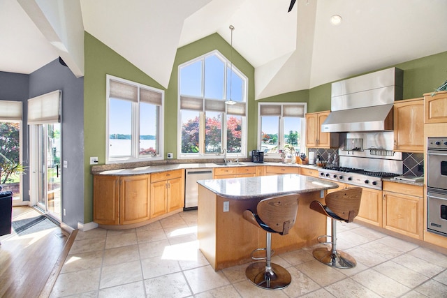 kitchen with stainless steel appliances, a center island, light stone counters, decorative backsplash, and wall chimney exhaust hood