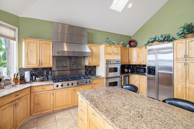 kitchen featuring stainless steel appliances, lofted ceiling with skylight, light stone counters, and range hood