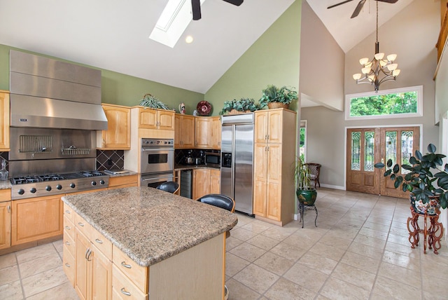 kitchen with stainless steel appliances, a kitchen island, ceiling fan with notable chandelier, and light stone counters