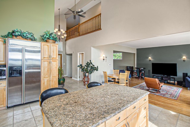 kitchen with stainless steel appliances, a center island, light stone counters, ceiling fan with notable chandelier, and light brown cabinets